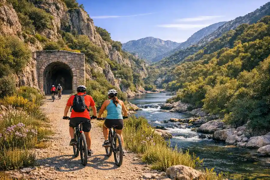 Ciclistas recorriendo la Vía Verde del Serpis junto al río y túnel de piedra en un paisaje natural de montaña